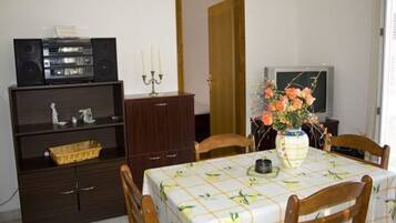 Un comedor con una mesa dispuesta para cuatro personas, un aparador de madera oscura con estantes, un televisor y un florero con flores.