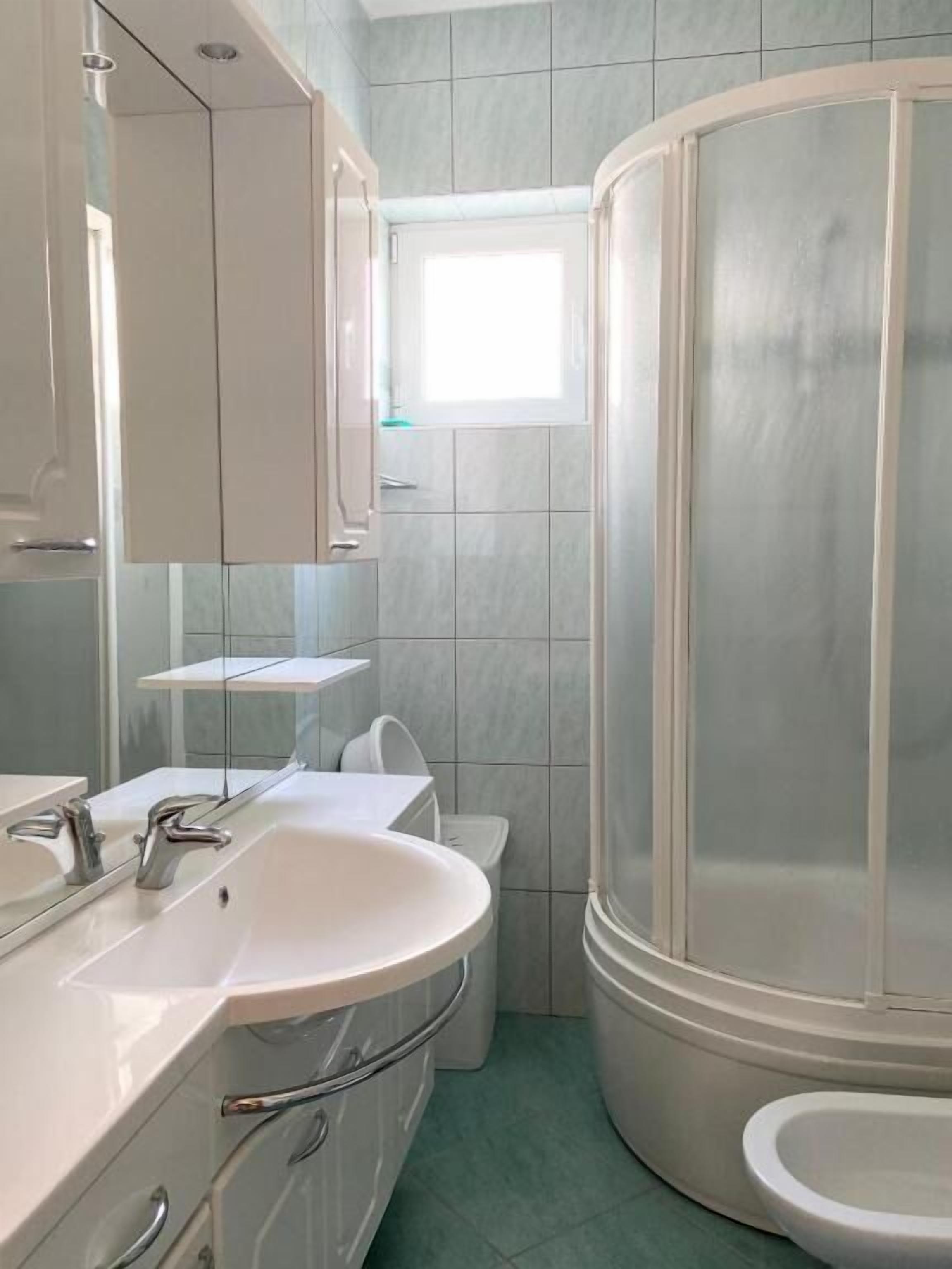 A modern bathroom with a white sink, mirror, and shower enclosure.
