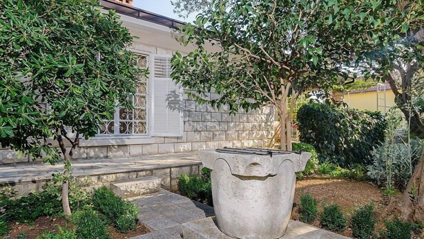 Un jardin avec un grand bac à fleurs, un mur en pierre et un bâtiment doté d’une fenêtre et d’une porte.