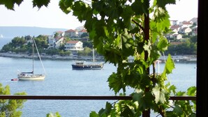 Blick auf die Küste mit Booten auf dem Wasser, Häuser im Hintergrund und ein Balkon mit Grünpflanzen.
