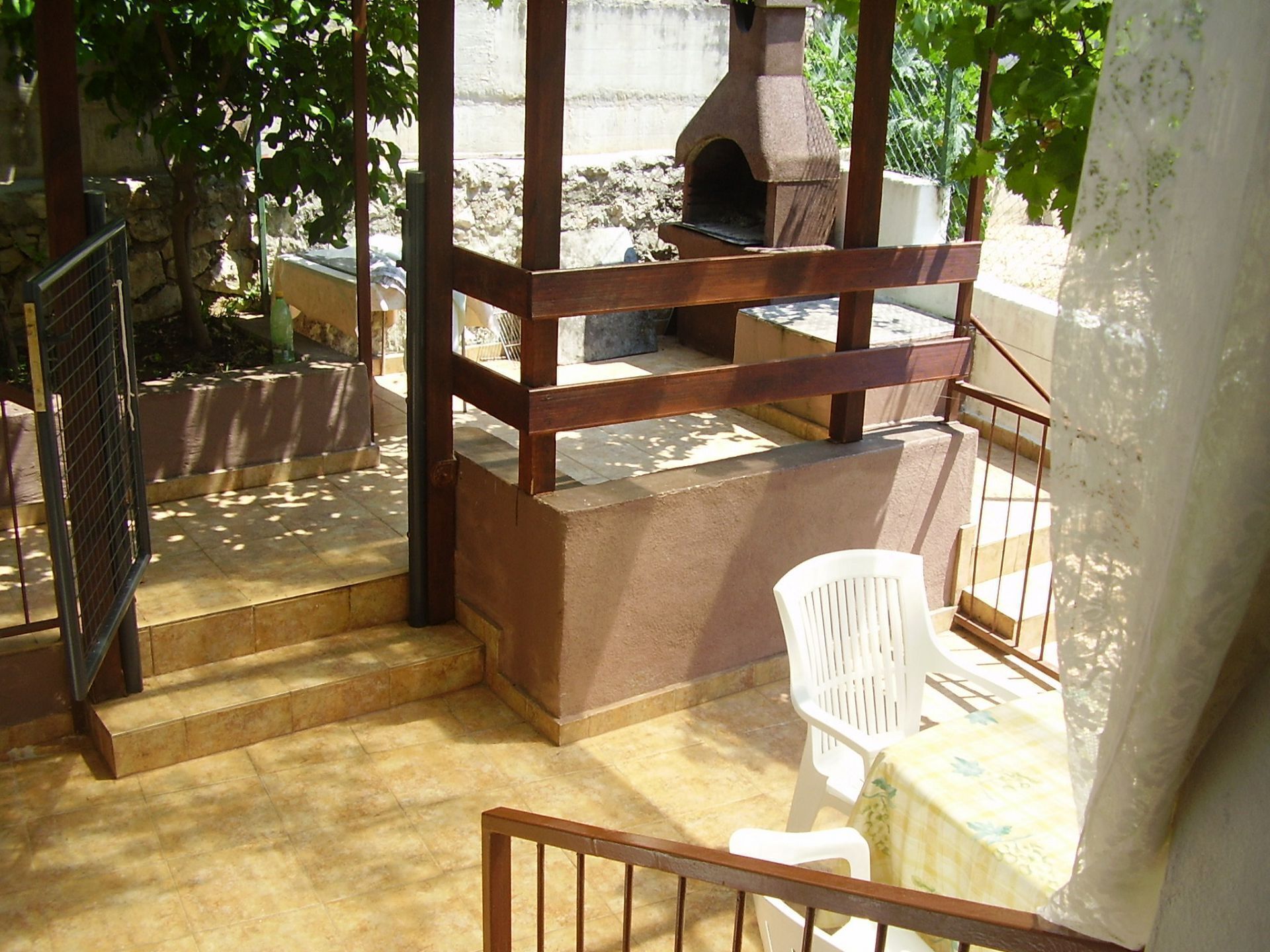 A covered outdoor area with a stone oven, steps leading to a patio, and a white plastic chair.