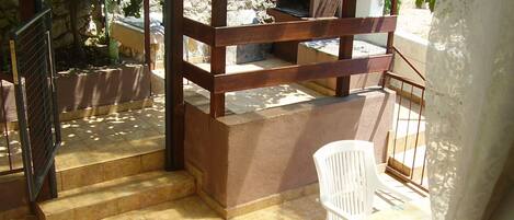 A covered outdoor area with a stone oven, steps leading to a patio, and a white plastic chair.