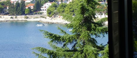 A coastal town with buildings along the shore, a boat on the water, and a tree in the foreground.
