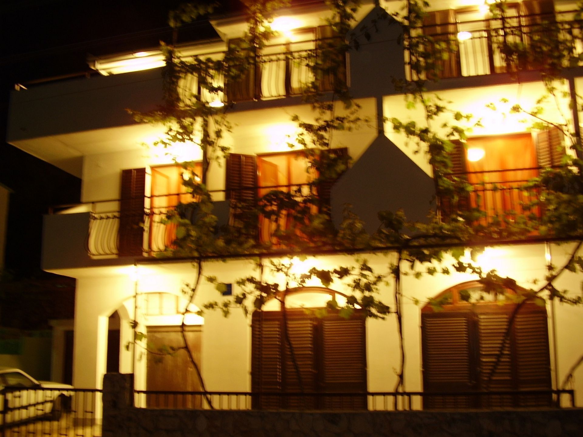 A multi-story building with balconies, illuminated windows, and a stone facade.