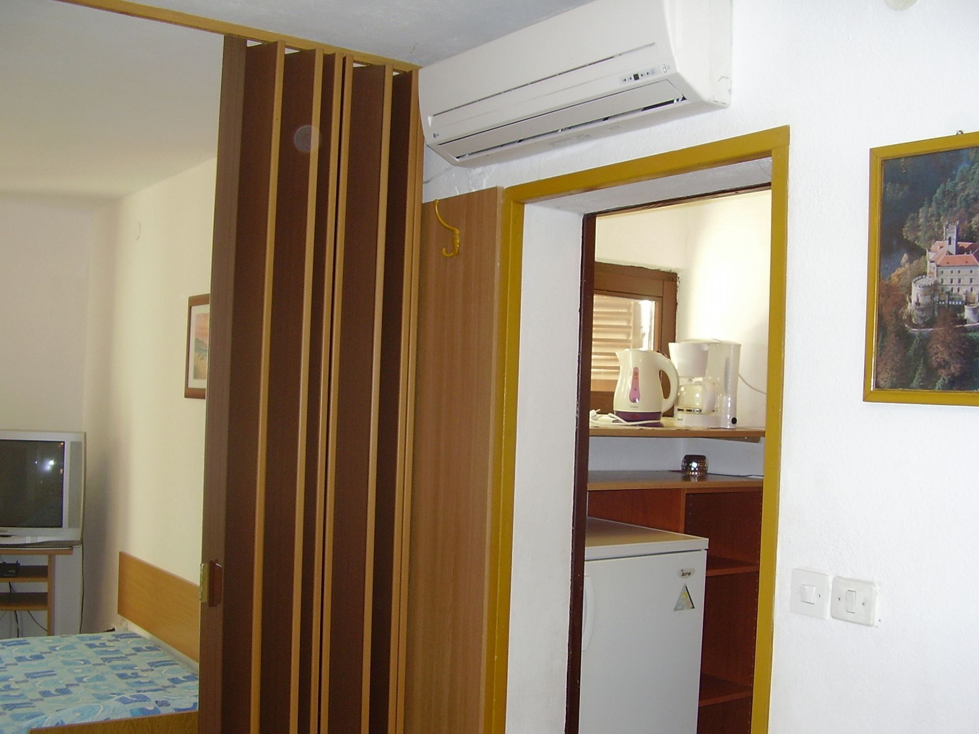 Een kamer met een bed, een televisie, een airconditioner, een koelkast en een schilderij aan de muur.