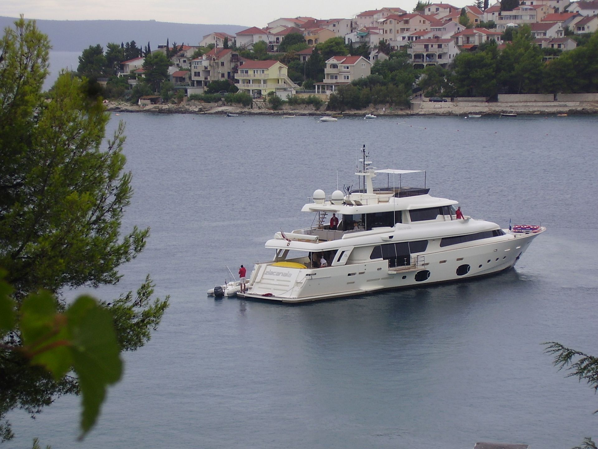 Eine große Yacht liegt an einem Anlegesteg in der Nähe eines Wohngebiets mit Häusern im Hintergrund.