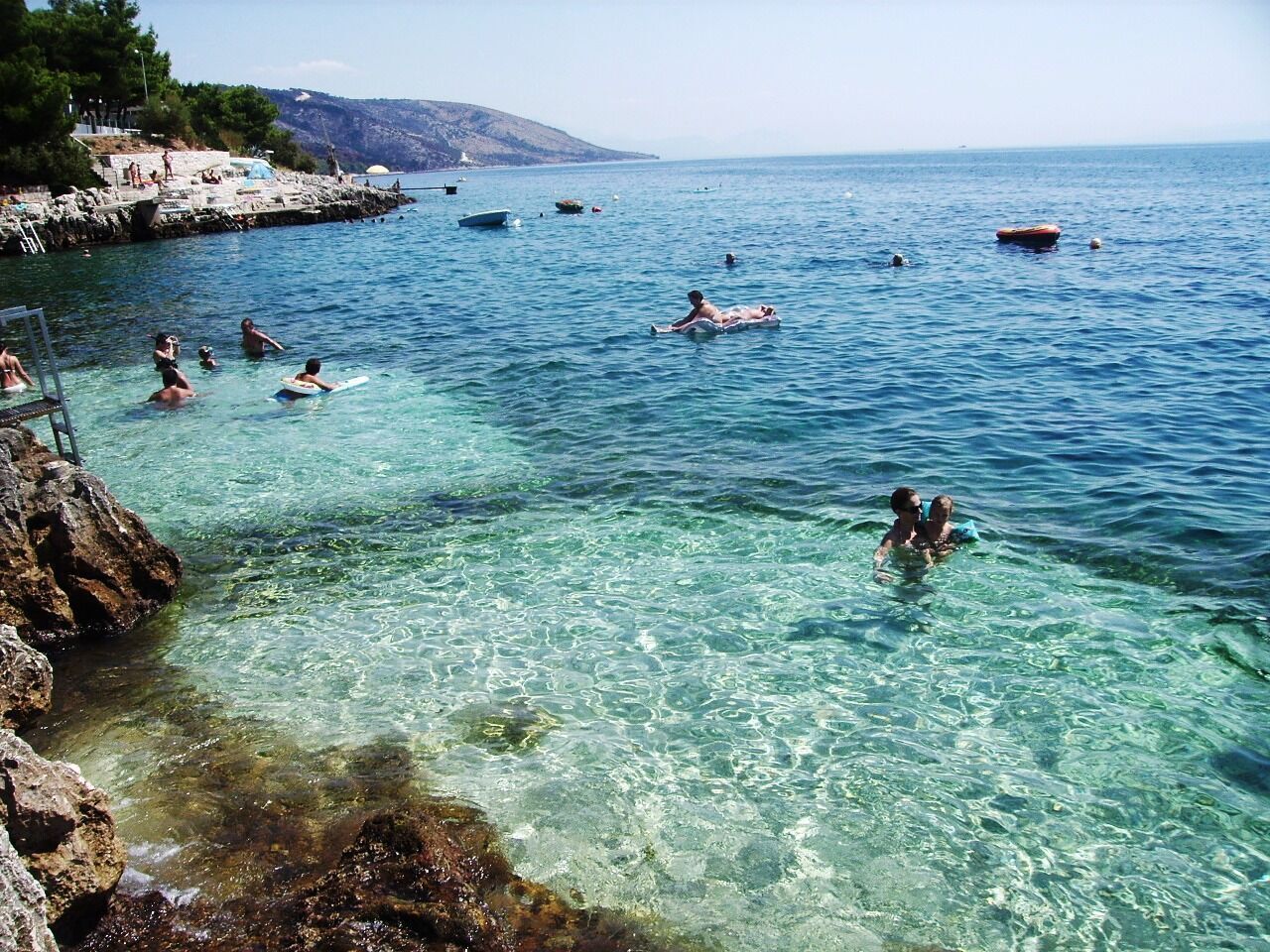 A coastal area with clear waters, rocky shore, and boats.