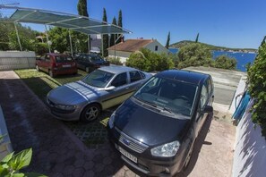 A parking area with three cars, a covered outdoor seating area, and a view of the sea. - Apartments Milans (Rogoznica)