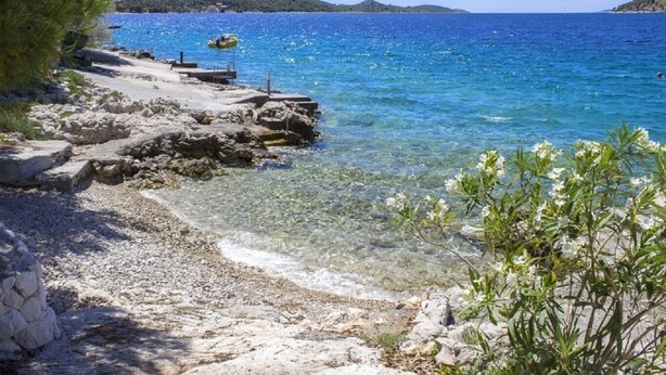 A rocky beach with clear water, a small boat, and distant hills. - Apartments Milans (Rogoznica)