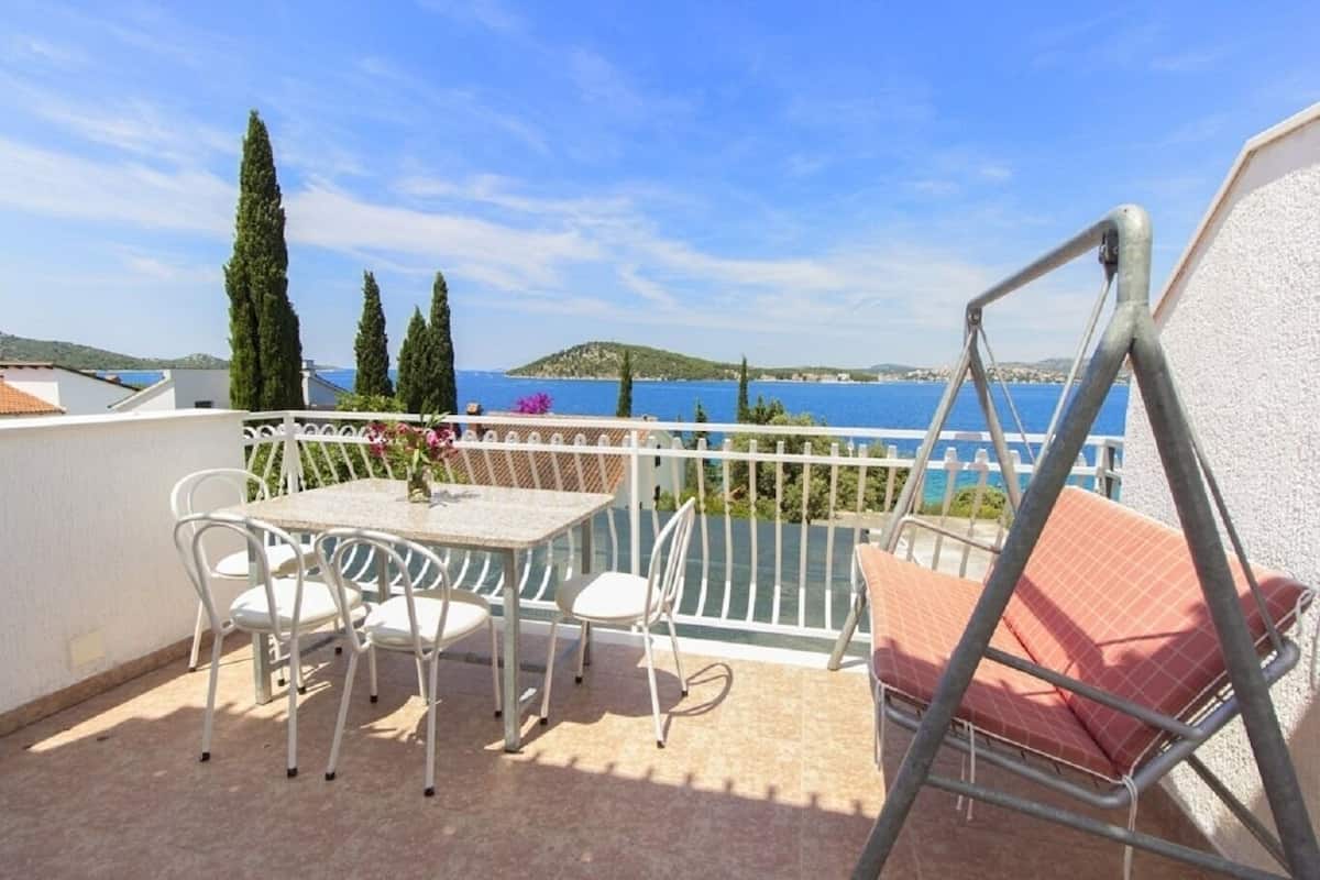 A terrace with a table and chairs, a swing, and a view of the sea and hills.