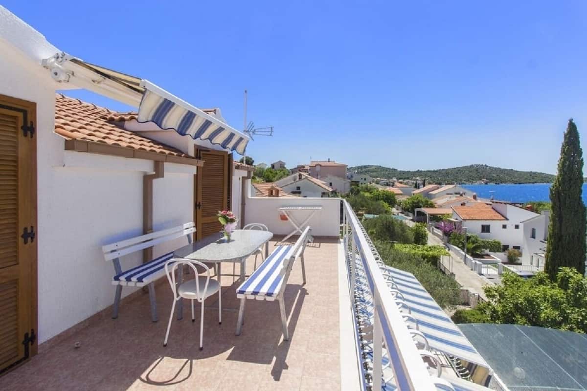 A balcony with a table and chairs, a view of the sea, and a tiled roof.