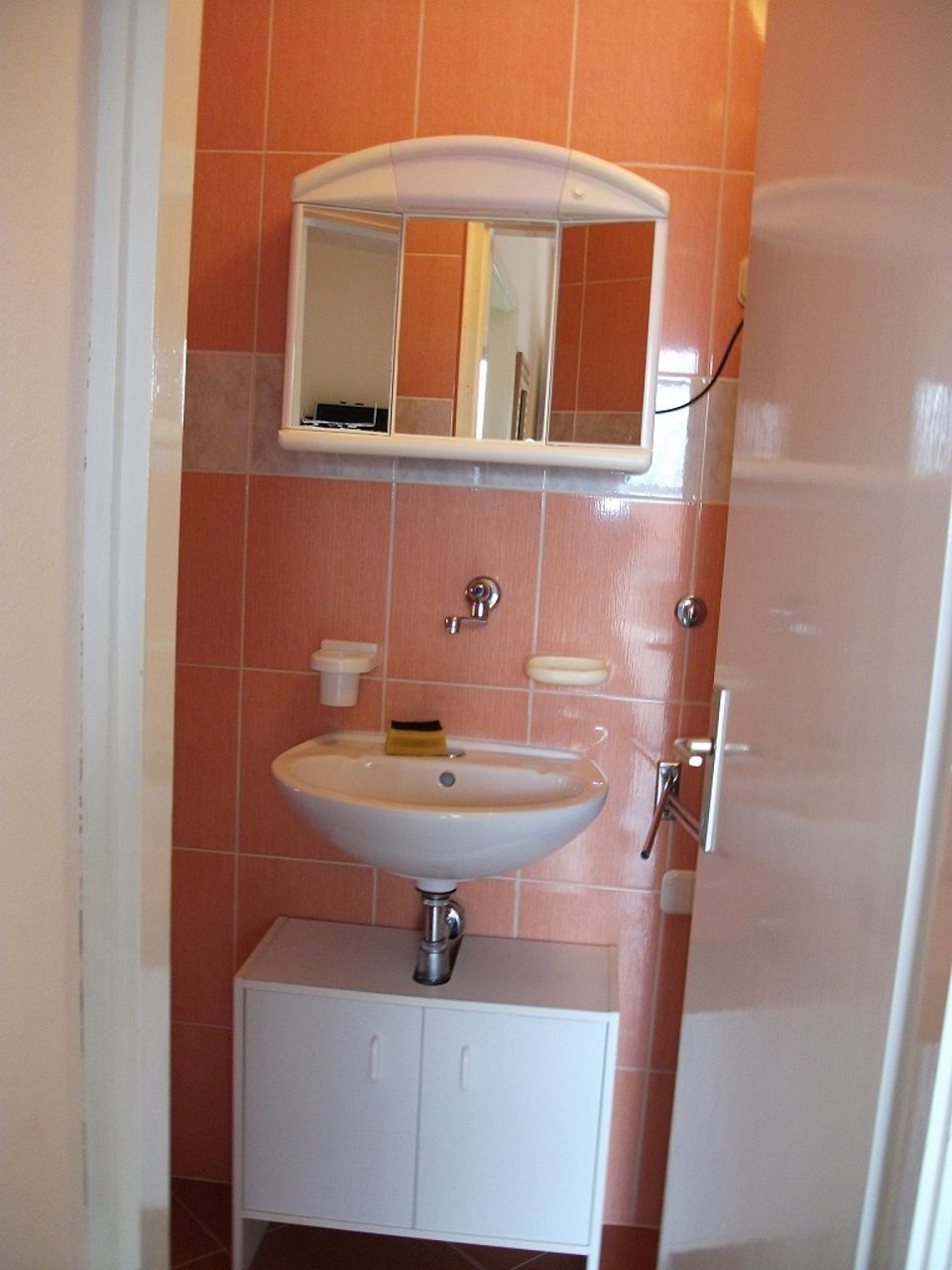 A bathroom with a white sink, a mirror above it, and a cabinet below.