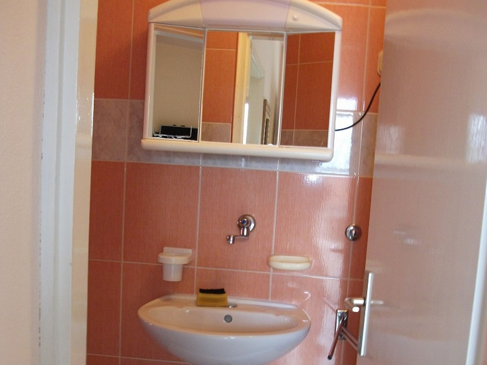 Ein Badezimmer mit einem weißen Waschbecken, einem Spiegel darüber und einem Handtuchhalter zur Rechten.