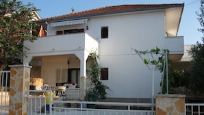 A two-story house with a white exterior, stone pillars, and a tiled roof. - Apartment Dusko (Obrovac)