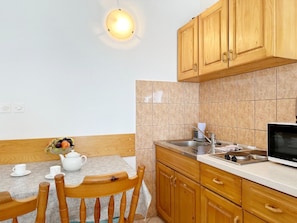A kitchen with wooden cabinets, a microwave, a sink, and a table with chairs. - Apartments Mira (Gradac)