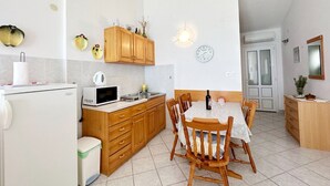 Een compacte keuken met houten kastjes, een magnetron, een spoelbak en een eettafel met stoelen.