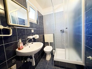 A bathroom with a sink, toilet, and glass-enclosed shower. - Apartments Mira (Gradac)
