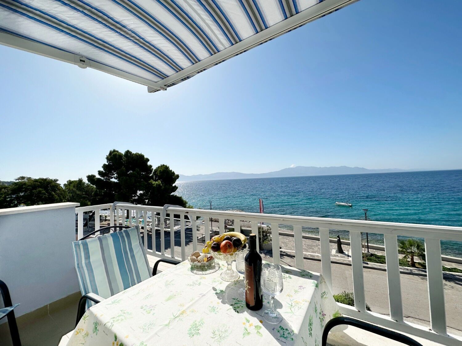A balcony with a table set for two, overlooking a coastal view with a clear sky and calm sea.
