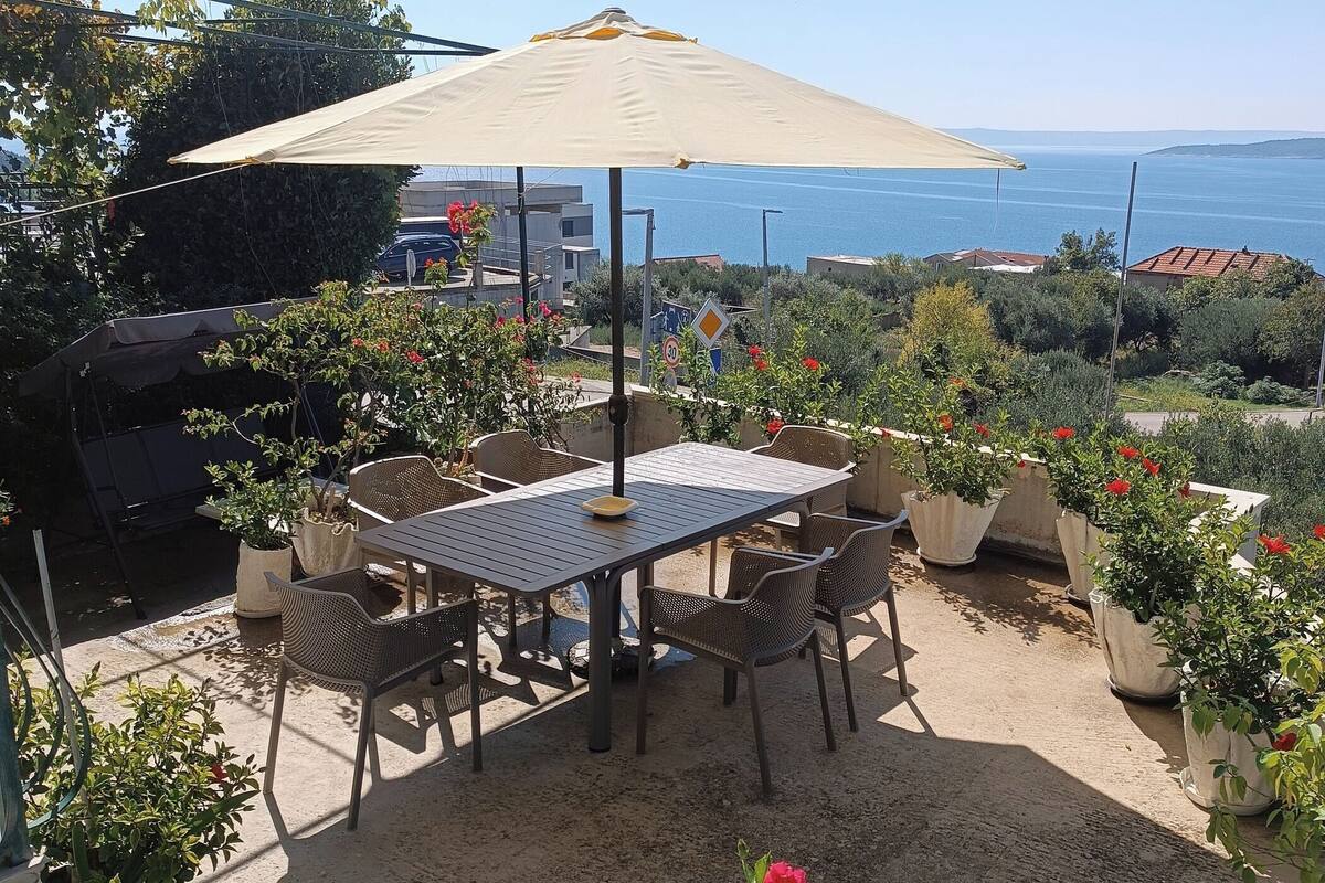 An outdoor patio with a table and chairs, surrounded by potted plants and a view of the sea.
