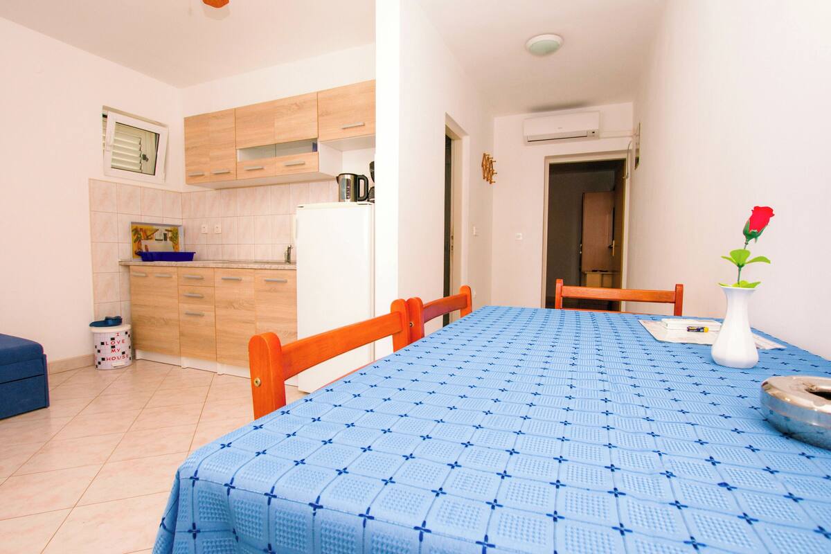 A compact kitchen with wooden cabinets, a white refrigerator, and a blue tablecloth-covered dining table.