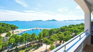 Ein Balkon mit Blick auf eine Küstenlandschaft, darunter ein Strand, Boote und ein klarer Himmel.