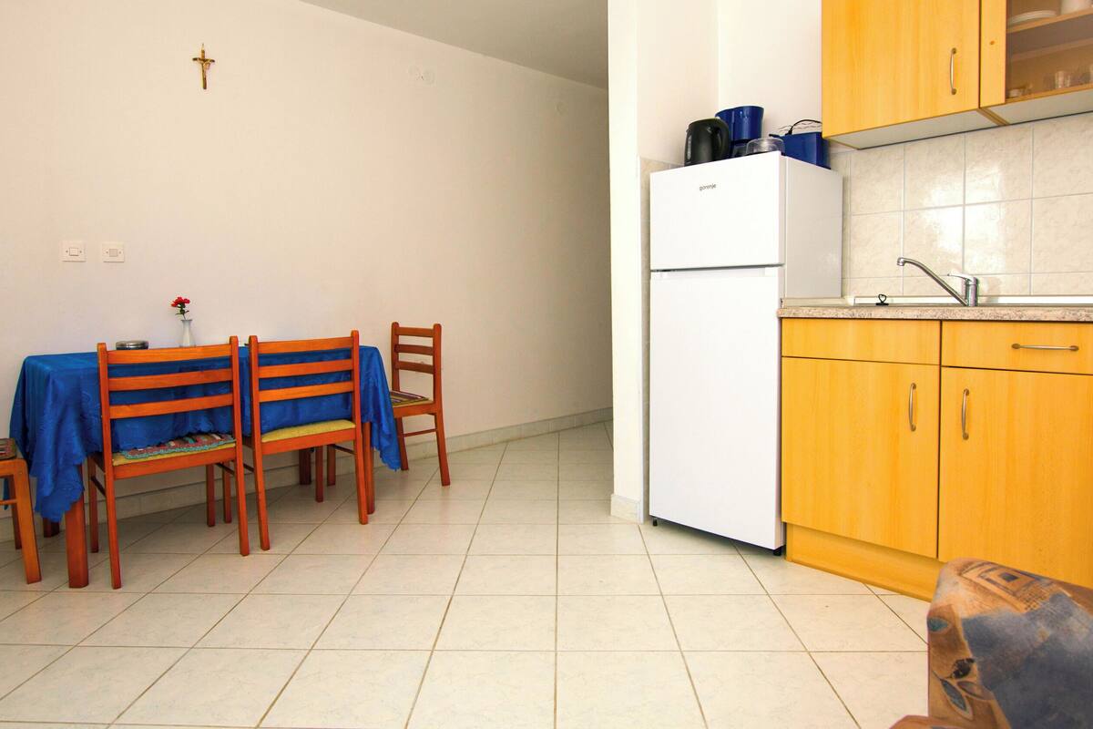 A small, clean room with a dining table, chairs, a white refrigerator, and wooden cabinets.
