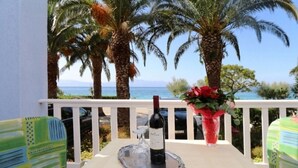 Un balcón con una mesa preparada para dos personas, una botella de vino, una copa y un jarrón con flores.