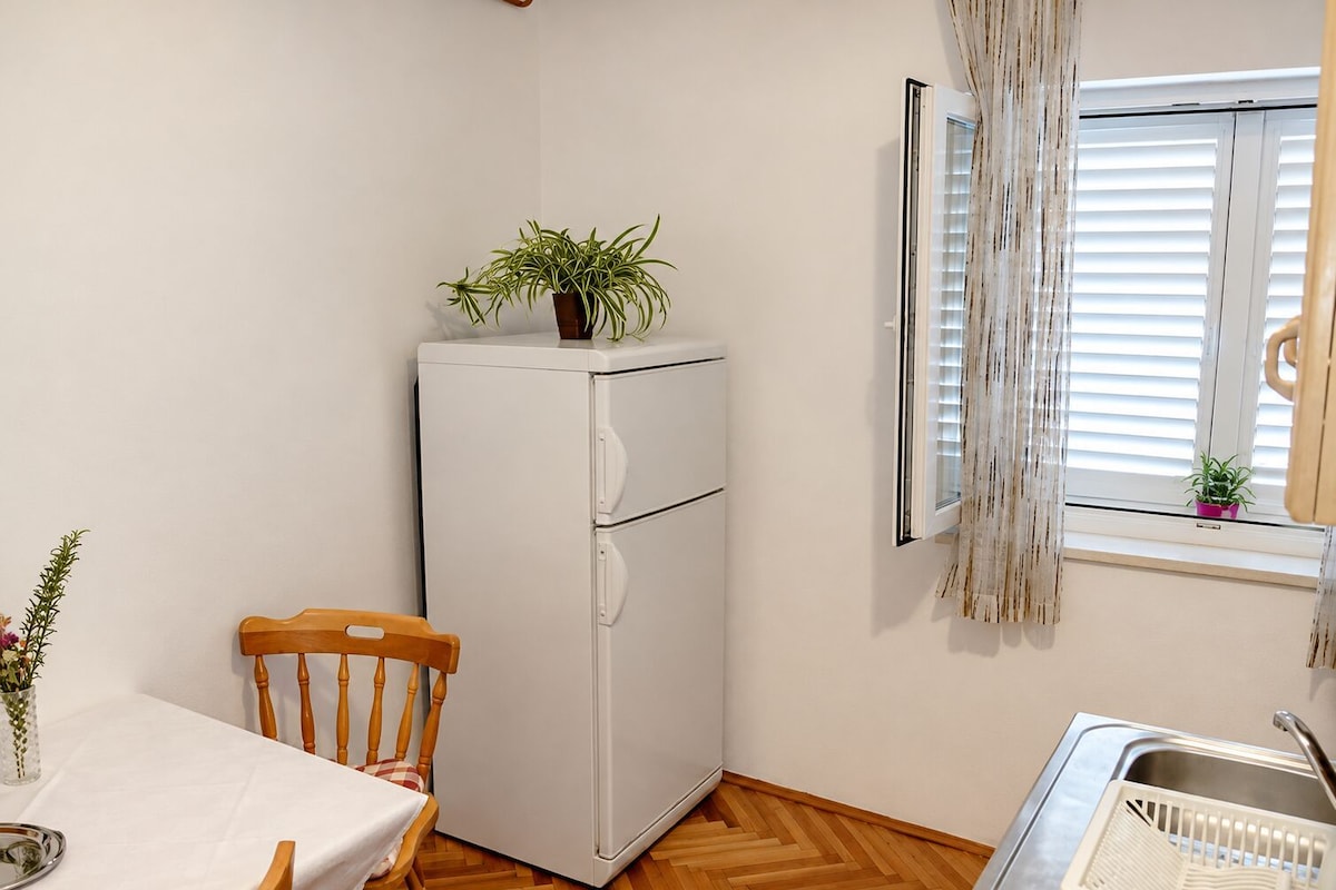A compact kitchen with a white refrigerator, wooden dining table, and chairs.