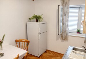 A compact kitchen with a white refrigerator, wooden dining table, and chairs. - Apartment and Rooms Tomo 1 (Gradac)
