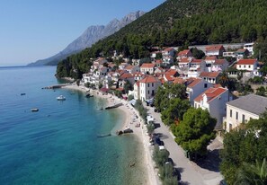 A coastal town with buildings along the beach and mountains in the background. - Apartment and Rooms Tomo 1 (Gradac)