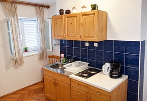 A compact kitchen with wooden cabinets, a sink, a stove, and a coffee maker. - Apartment and Rooms Tomo 1 (Gradac)