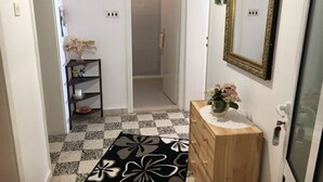Un estrecho pasillo con piso a cuadros, un aparador de madera con un florero y un espejo en la pared.