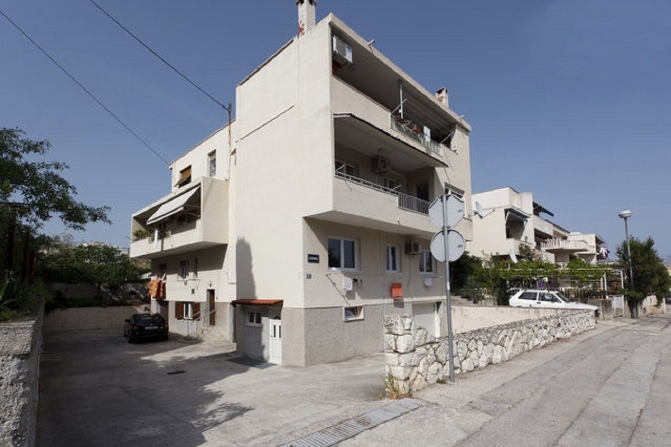A multi-story residential building with balconies, a stone wall, and a parked car.