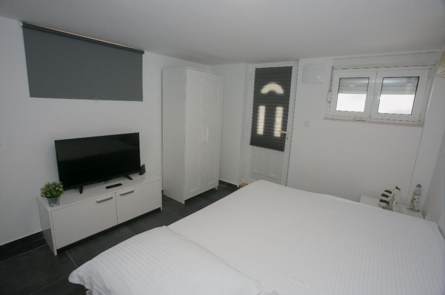 Un dormitorio con una cama grande, un televisor sobre un mueble blanco, un armario y una ventana con persianas.