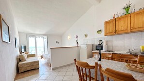 A modern kitchen with wooden cabinets, a dining area with wooden chairs, and a living room with a sofa and a TV. - Apartments Tomo (Gradac)