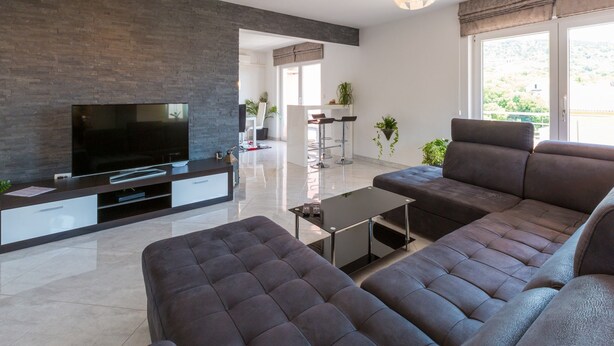 Una sala de estar moderna con un televisor de pantalla plana, sofás oscuros, una mesa de centro y un ventanal con vistas.