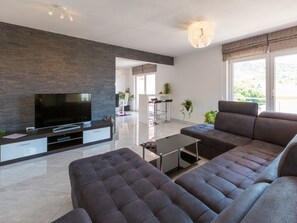 A modern living room with a flat-screen TV, dark sofas, a coffee table, and a large window with a view. - Apartment Black@white (Novi Vinodolski)