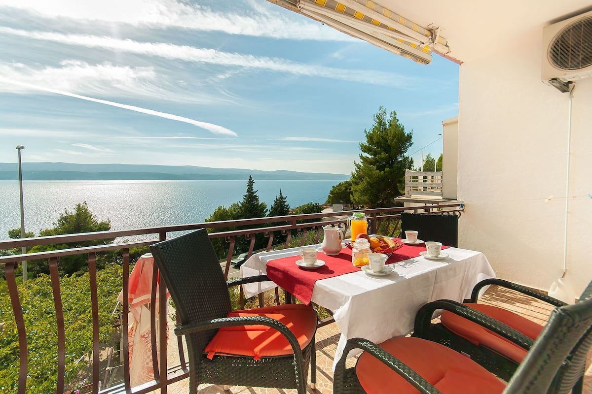 Un balcon avec une table préparée pour le petit-déjeuner, offrant une vue sur un lac et des montagnes.