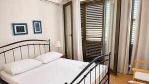 Een netjes opgemaakt bed met witte lakens, een bedlampje en twee ingelijste foto’s aan de muur.