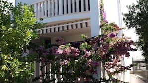 Un edificio bianco con un balcone, immerso nel verde e circondato da piante fiorite.