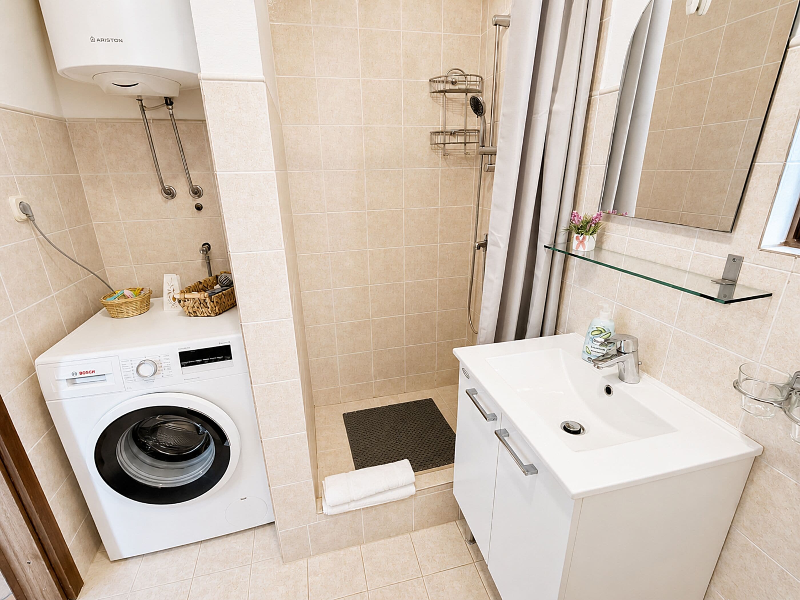 A compact bathroom with a Bosch washing machine, a glass shelf, and a mirror.