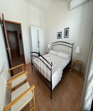 A bedroom with a bed, two bedside tables, a chair, a wardrobe, and an air conditioning unit. - Apartment Zeljka (Rogoznica)