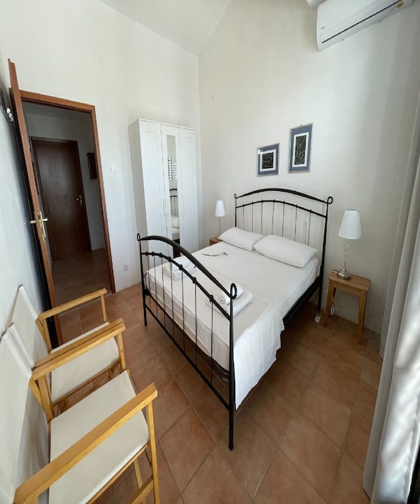 A bedroom with a bed, two bedside tables, a chair, a wardrobe, and an air conditioning unit. - Apartment Zeljka (Rogoznica)