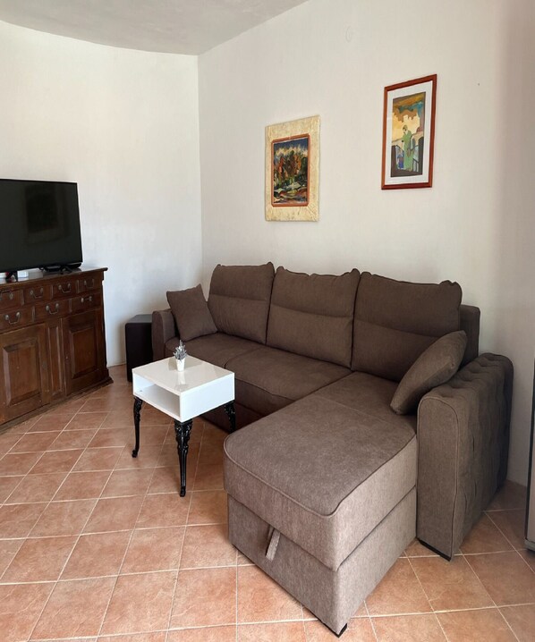 A living room with a sectional sofa, a coffee table, a TV on a wooden cabinet, and two framed pictures on the wall. - Apartment Zeljka (Rogoznica)