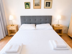 A neatly made bed with white linens, two bedside tables with lamps, and three framed pictures on the wall. - Apartment Zeljka (Rogoznica)