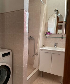 Ein Badezimmer mit Waschmaschine, Dusche mit Glastür, Waschbecken und Spiegel.