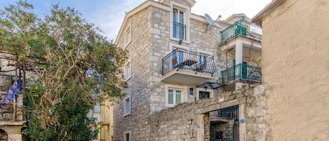 A narrow street with stone buildings, a tree, and a balcony with a metal railing.