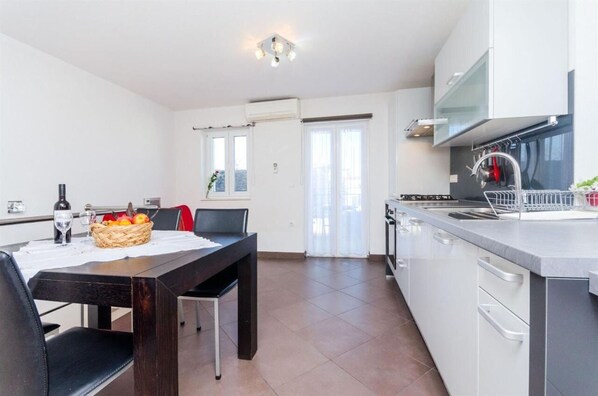 Een moderne keuken met witte kastjes, een eettafel met stoelen en een mand vol fruit.