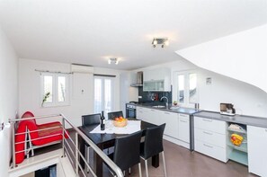 Een moderne keuken met witte kasten, een eethoek met een tafel en stoelen, en een rode bank in een slaapkamer met een vide.