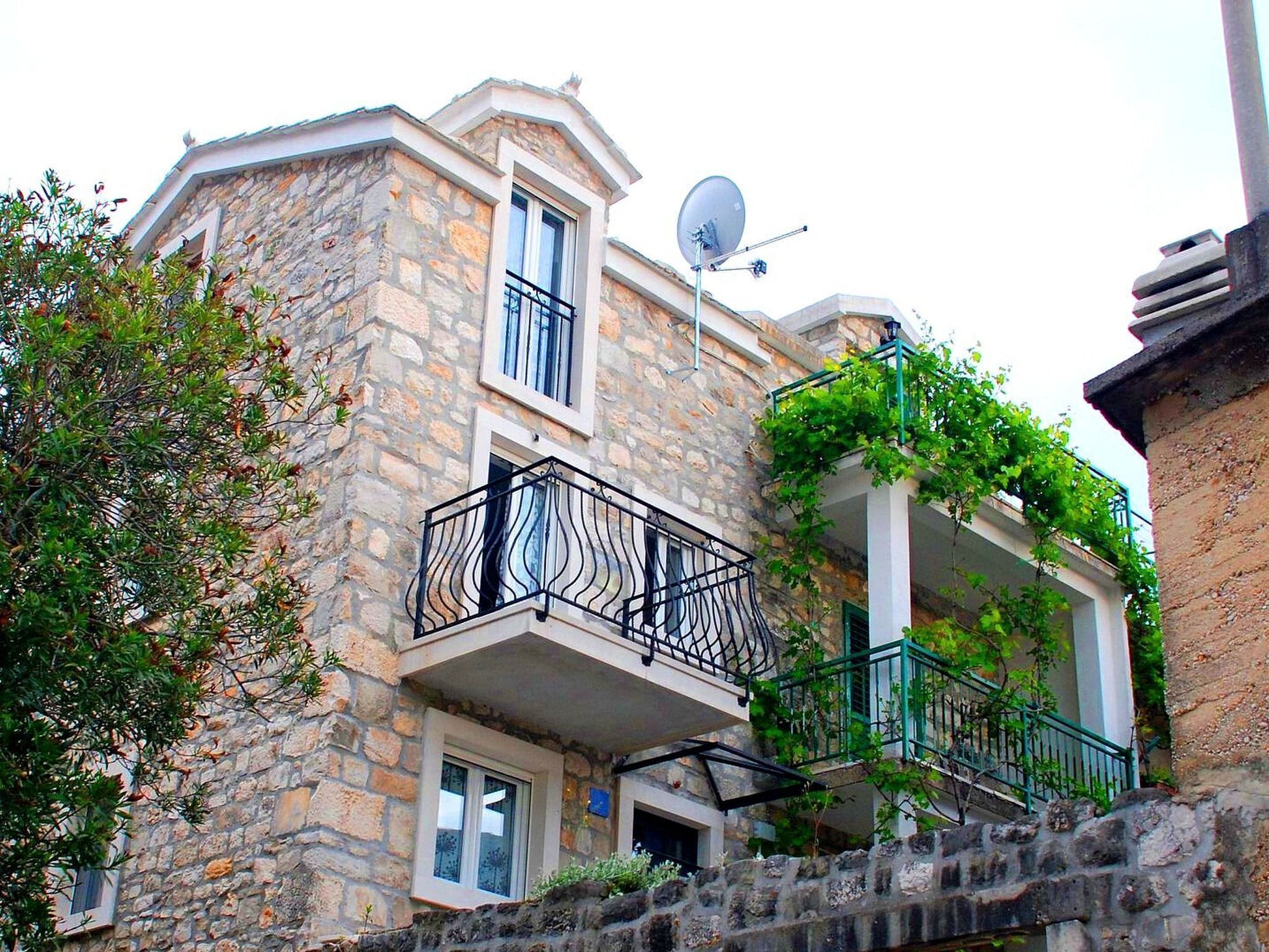 Un edificio de piedra con balcón, antena parabólica y escalera que lleva a otro nivel.